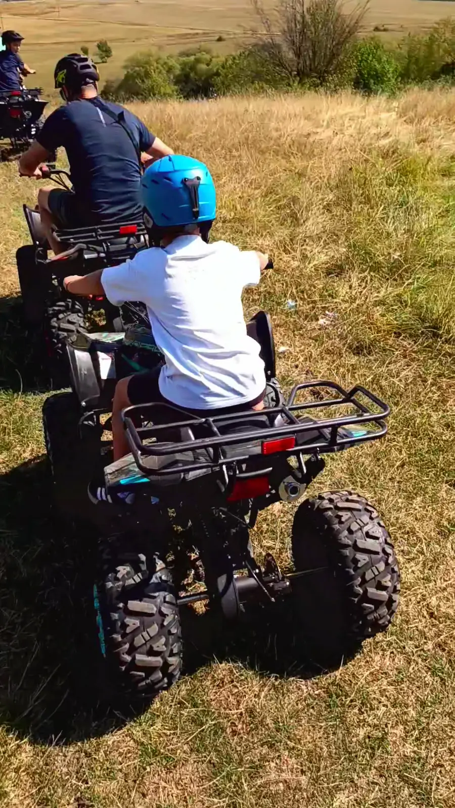 Copil cu cască albastră pe ATV, pe o pajiște uscată de vară