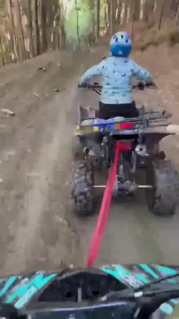 Un băiat cu cască tractează în glumă ATV-ul nostru cu o chingă